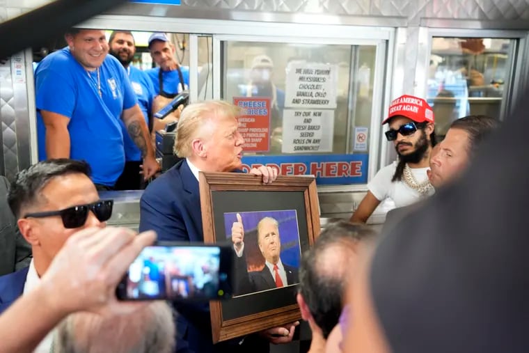 Former President Donald Trump, holding a framed photo of himself, greets customers and staff at Tony & Nick's as rapper QT-7 Quanny (second from right) looks on Saturday in Philadelphia.