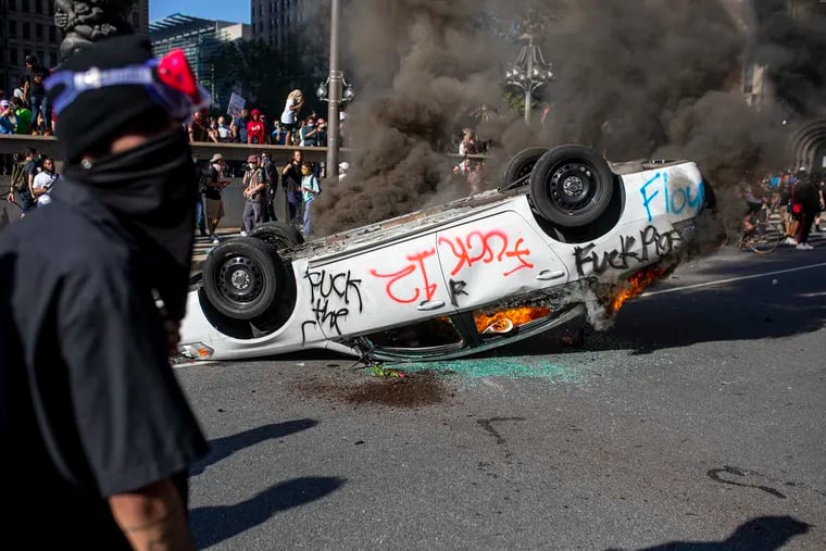 A protester walks by as a flipped over police vehicle is set on fire outside City Hall during protests in Philadelphia in response to the police killing of George Floyd on May 30, 2020.