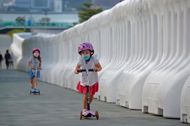 Kids wearing masks to protect against the coronavirus, play beside the water-filled barriers outside the Hong Kong Government Office on Aug. 20. A new report found that Children and teens make up a small but steadily growing proportion of COVID-19 cases in the U.S. (AP Photo/Kin Cheung)