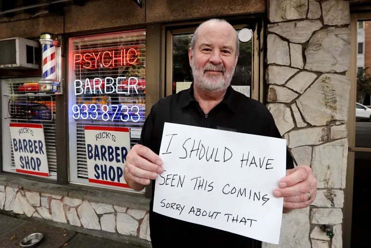 In this photo taken Thursday, June 4, 2020, barber Rick Cook holds the sign he's been playfully displaying in his "Psychic Barber" shop, closed because of the coronavirus outbreak, in Seattle.  The U. S. economy added 1.8 million jobs in July, but that was less than half the jobs added in June.  (AP Photo/Elaine Thompson)