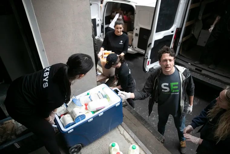 Evan Ehlers, right, founder of Sharing Excess, a Philadelphia-based nonprofit that helps connect grocery stores and restaurants with surplus food to hunger-relief organizations with storage space, lifts up milk to weigh and load in a truck from Saxby's headquarters in Center City Philadelphia on Tuesday, March 17, 2020. Sharing Excess has received much more food than usual due to restaurants closing from the spread of the coronavirus.