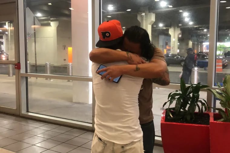 Brothers Saroun Khan, in dark shirt, and Sarith Khan, in orange Flyers hat, embrace at Philadelphia International Airport on Thursday night after Saroun arrived in Philadelphia from Texas, released after 13 months in ICE detention. Saroun, who is a few years older, still faces deportation, but gaining freedom represents a big step forward in his case.