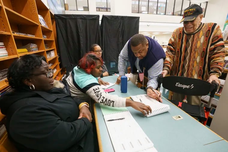 (From left) Patti Page-Walton, minority inspector; her daughter, Nichole Walton, majority inspector; and Sena Bowman, machine inspector, assist as John A. Reese III and his grandfather John A. Reese Sr. sign in to vote at the Lucien E. Blackwell West Philadelphia Regional Library last week.