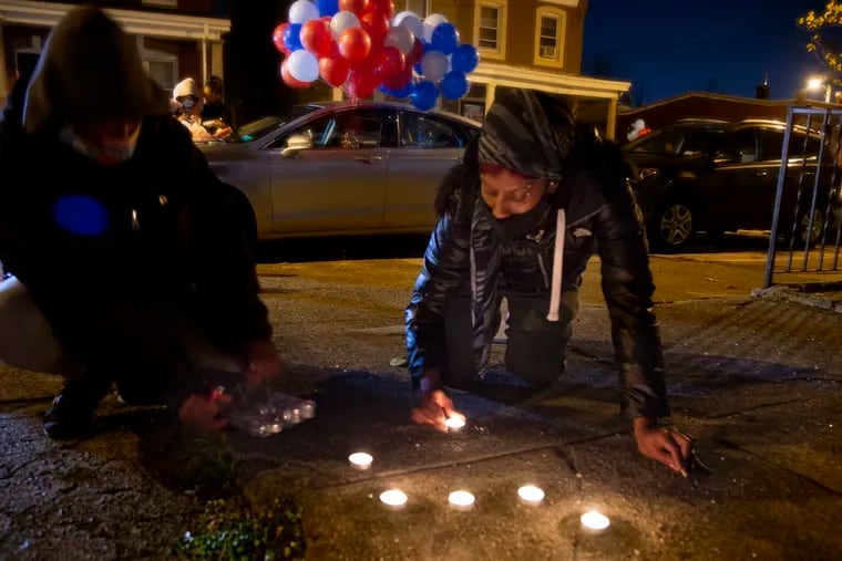 Asia Aziz, a neighbor and mother of a playmate of 12-year-old Sadeek Clark-Harrison, lights candles in the shape of his initials as the family prepares for a vigil outside their home Monday night.