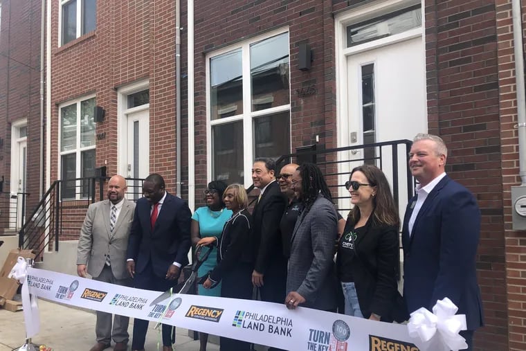 Mayor Cherelle L. Parker and Ms. Hinton, Turn the Key's 100th homebuyer, hold giant scissors as they prepare to cut a ceremonial ribbon in front of Hinton's hew Brewerytown rowhouse. Pictured, from left are Michael Ritter, senior vice president at Regency Furniture; City Council President Kenyatta Johnson; Parker; Hinton; Angel Rodriguez, executive director of the Philadelphia Land Bank; David Thomas, president and CEO of the Philadelphia Housing Development Corp.; City Councilmember Jeffrey Young Jr.; Brennan Tomasetti, co-founder and owner of Civetta Property Group; and Joe Hallinan, a vice president at WSFS.