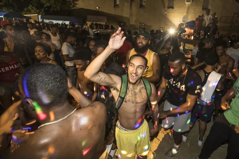 The parking lot of an auto repair garage in North Philadelphia was converted into a mini beach with sand, above ground pools, a wooden deck and beach furniture for a party on July 13, 2018. Ron Carroll, center, and others dance in a spray of colored lights.