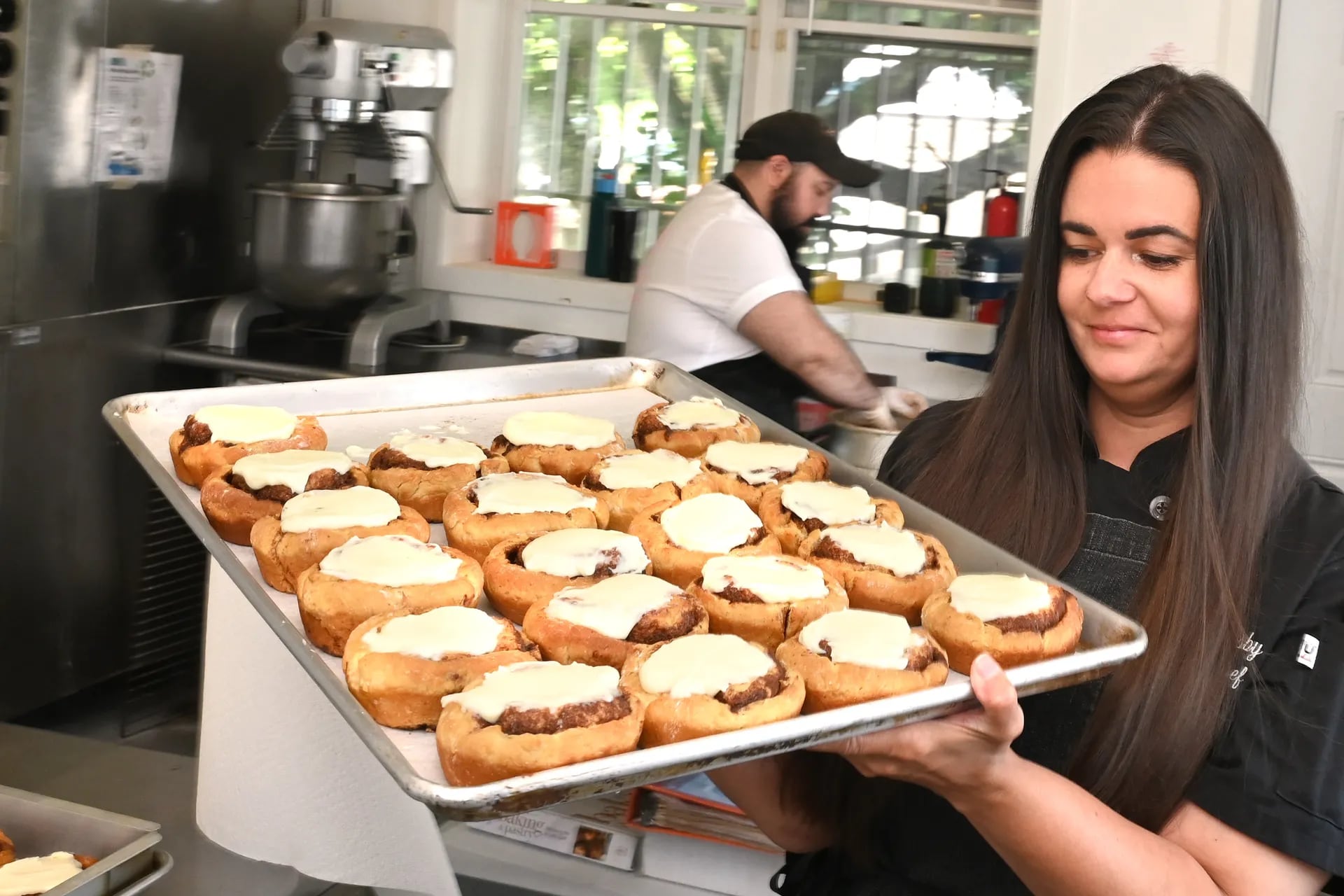 Chef owner Jenna Kisby carries a tray of cinnamon buns topped with cream cheese frosting at Kizbee’s Kitchen in Egg Harbor City, N.J. 