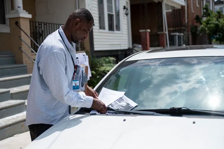 Eric Fair, a certified peer specialist for The Consortium, places a flyer on a car in Kingsessing in July 2023.