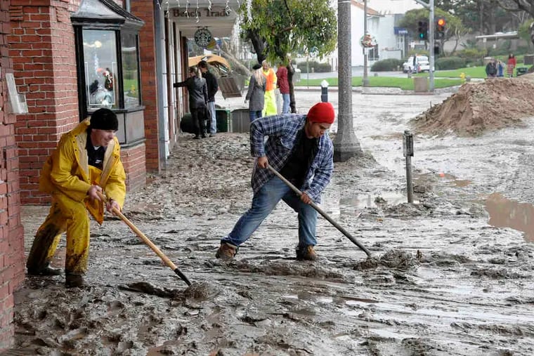 Workers shovel mud out onto the Pacific Coast Highway from the entrance to a movie theater in Laguna Beach, Calif. Los Angeles County residents were warned through Thursday to steer clear of contaminated water around storm drains, creeks, and rivers.