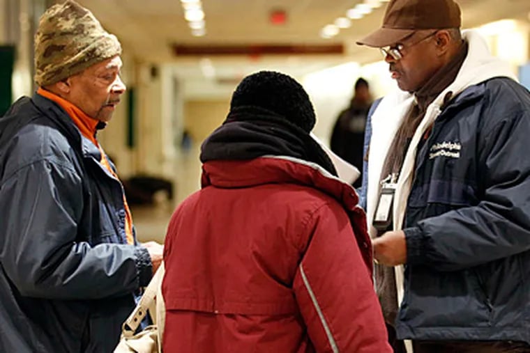 Mental Health Association outreach workers Jonathan Evans (left) and Stanley Crawley (right) talk with a homeless woman about shelter from the cold in the concourse of Suburban Station on Tuesday night. (Yong Kim/Staff)
