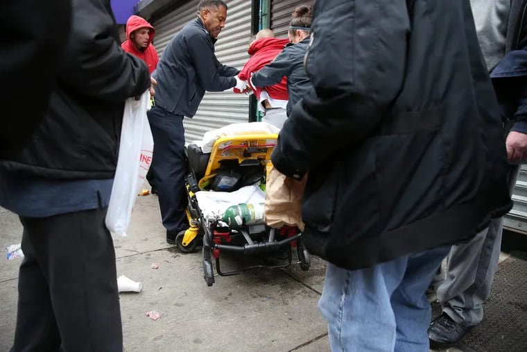 Deputy Commissioner for Emergency Medical Services Jeremiah Laster tries to help a heroin overdose victim (center) who could not be identified, get on a gurney after he was revived on Kensington Avenue in Philadelphia. The man refused and walked away from the scene.