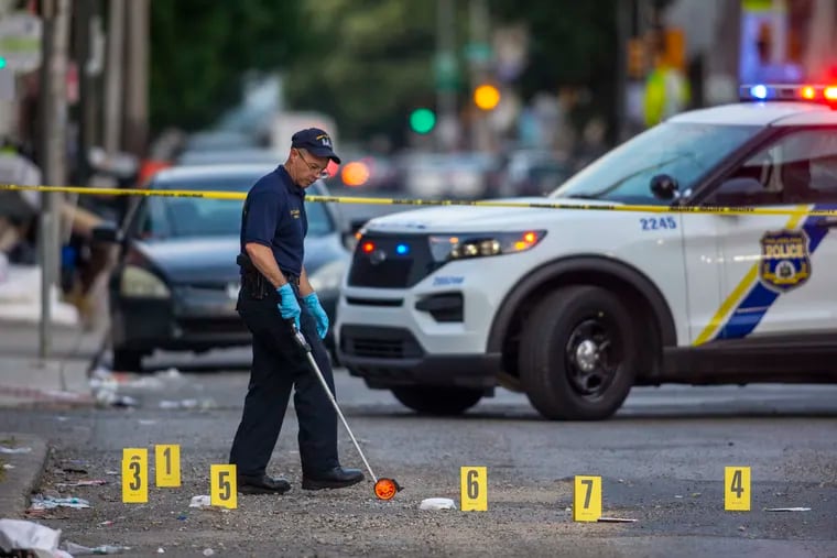 Crime scene officers gather and log evidence along Cecil B. Moore Avenue after a triple shooting left a woman dead and two men injured.