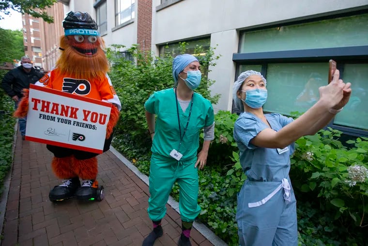 Members of the COVID Intensive Care Unit, Jana LaBarre (center) and  Ji Su Kim, (right), take a selfie as Flyers mascot, Gritty, arrives. Gritty visited the COVID Unit and led cheers for frontline responders as they made a shift change at Hospital of the University of Pennsylvania on May 12, 2020.