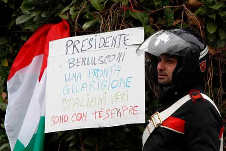 Outside Milan's San Raffaele Hospital , a paramilitary police officer is flanked by a sign, next to an Italian flag, that reads: &quot;President Berlusconi, get well soon. Real Italians are with you always.&quot;