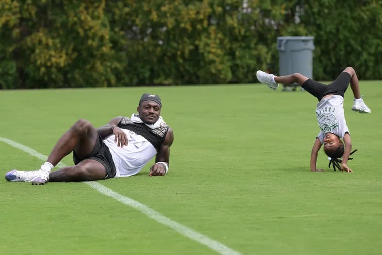 Eagles’ A.J. Brown rest as his daughter Jersee performs a handstand on Monday after a football training camp session at NovaCare Complex.