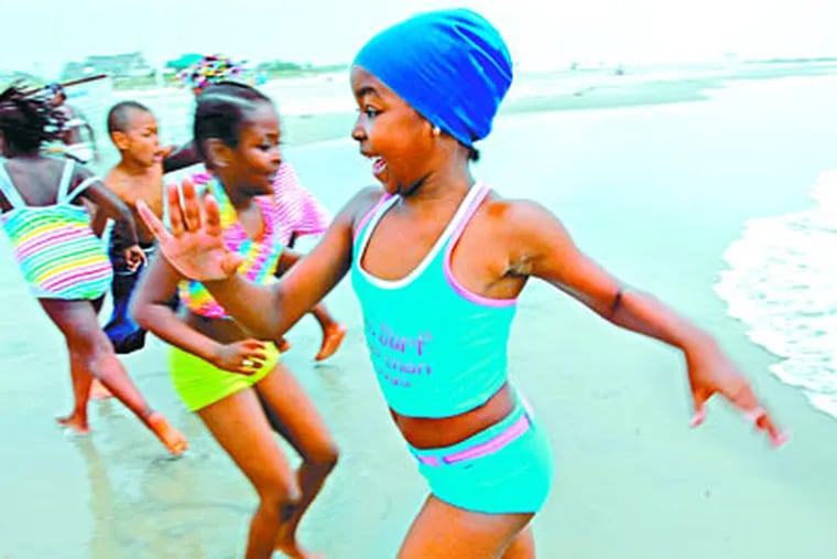 Chased by an incoming wave - and a very cold one at that - Esenje Murray (foreground) and friends retreated to high, dry ground at the beach in Ocean City. (APRIL SAUL / Inquirer Staff Photographer )