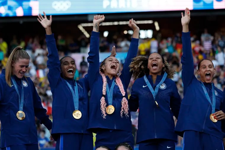 U.S. players (from left to right) Alyssa Naeher, Naomi Girma, Trinity Rodman, Casey Krueger, and Lynn Williams celebrate with their gold medals.