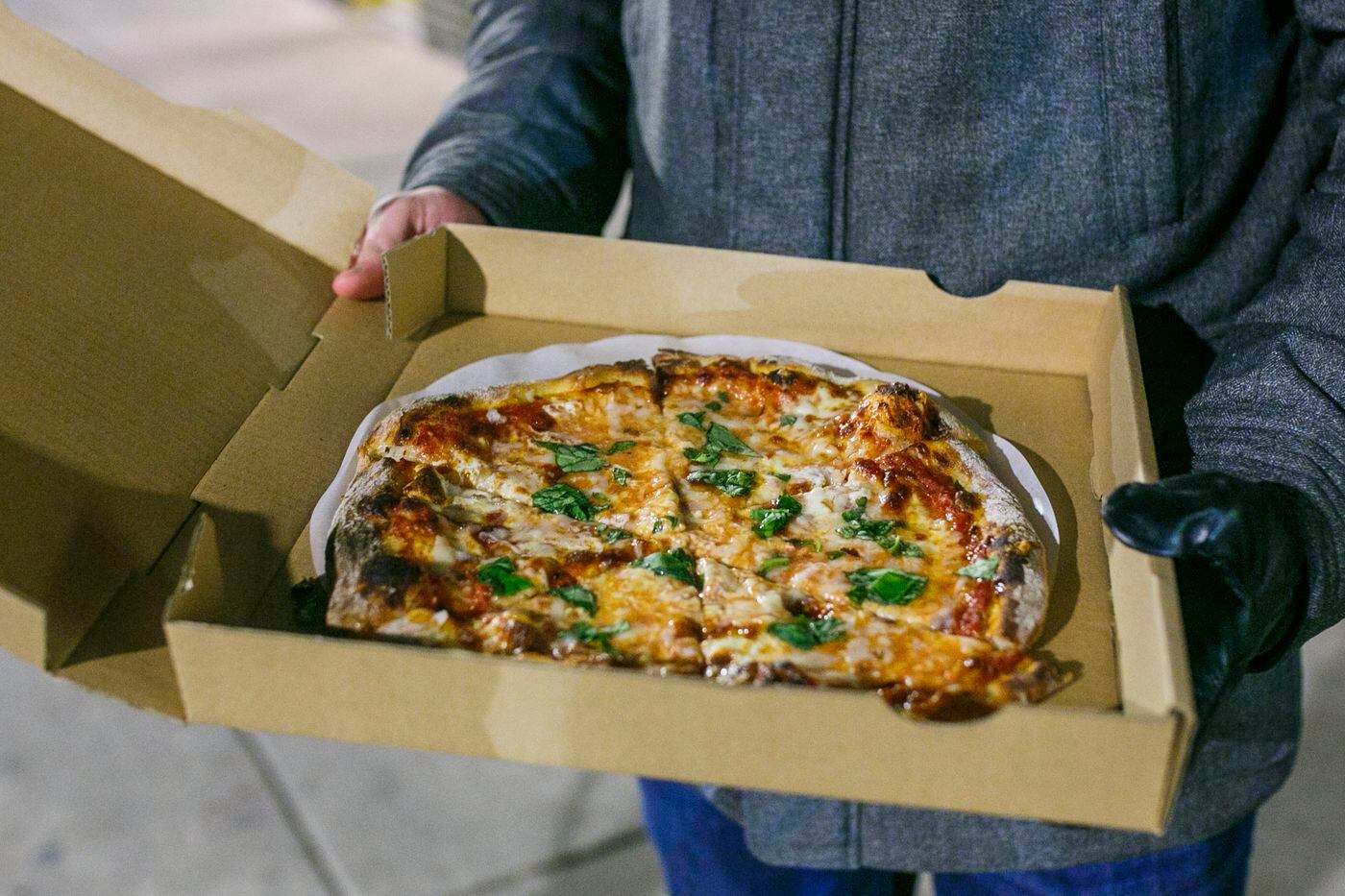 Josh Pezzulo of Philadelphia shows his Good Pizza pizza, which he picked up outside of Ben Berman's Center City apartment.