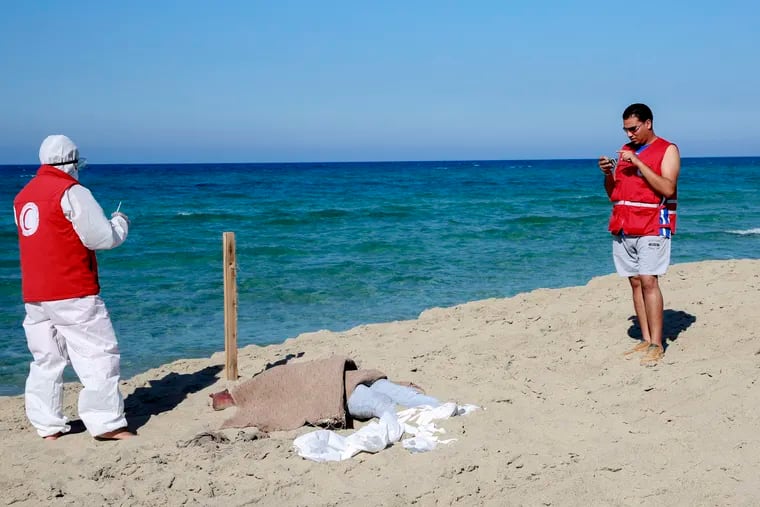 Libyan Red Crescent workers stand around a body of a drowned migrant near the city of Khoms, some 60 miles east of Tripoli, Libya, on Friday, July 26, 2019. Libya's coast guard recovered dozens of bodies of Europe-bound migrants who perished at sea as search operations continued Friday, a day after up to 150 people, including women and children, went missing and were feared drowned after their boats capsized in the Mediterranean Sea.