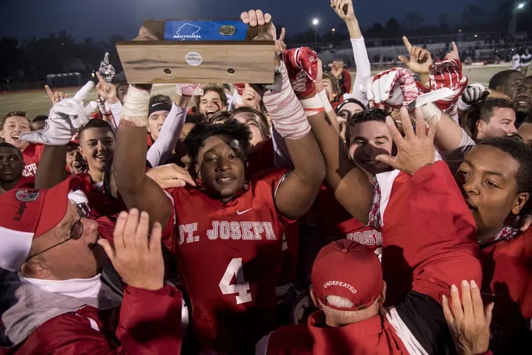 St. Joseph High’s Qwahsin Townsel, surrounded by his teammates, holds up the championship trophy as the NonPublic Group 2 champs after they beat Mater Dei.