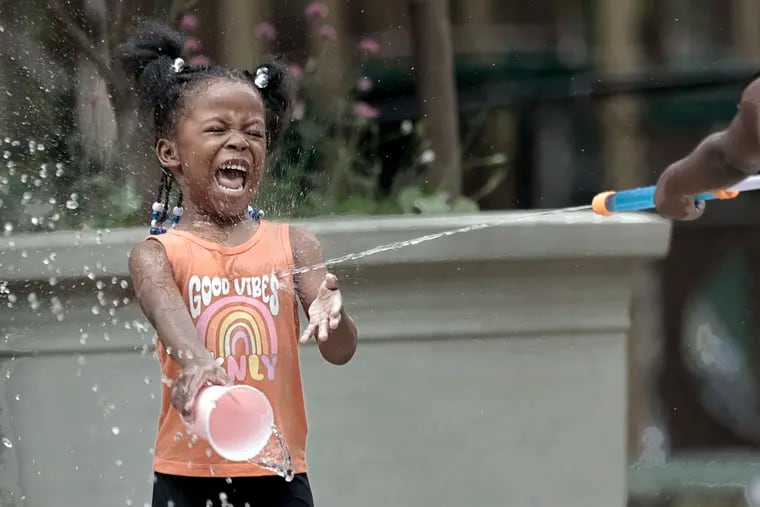 Kaliah Burgin, 4, screams good vibes as her older sister Ashia Burgin, 6, (right) sprays her with water from the water blaster while playing in the spray ground at Wharton Square Playground in the Point Breeze section of Philadelphia on Sunday.