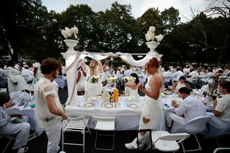 Zach Lutz (left) of Philly created this setup for his table. Annie Rulli of Haddon Twp., (center) estimates she has been to 10 Dîner en Blanc events. Jess Flamm of Philadelphia joins them for the 11th Dîner en Blanc at Memorial Hall in Fairmont Park in Philadelphia on Thursday, Aug. 10, 2023.