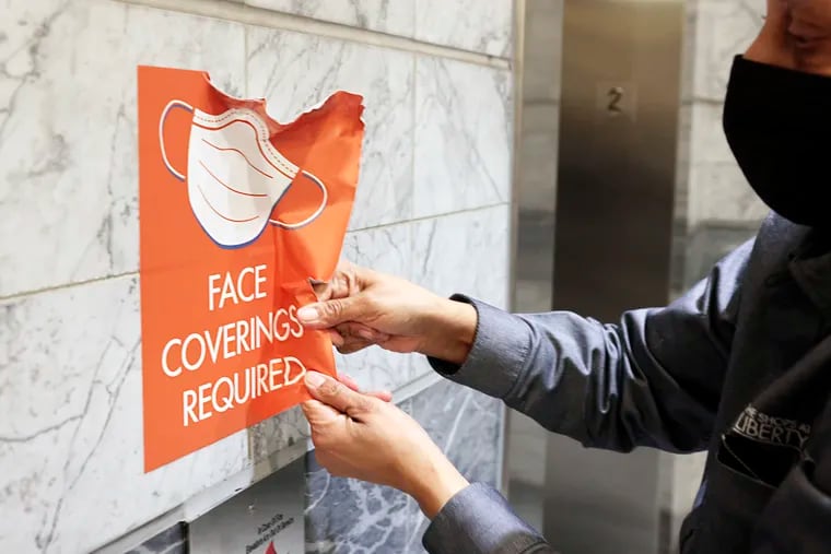 Paula Johnson, who works for Arthur Jackson Janitorial Services, removed a “FACE COVERINGS REQUIRED” sign from Liberty Place in Philadelphia on March 2.