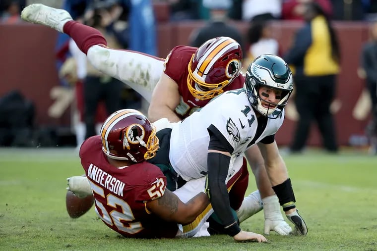 Eagles quarterback Carson Wentz fumbles the football as he is hit by Washington’s Ryan Anderson, left, and Matt Ioannidis, center, in the Philadelphia Eagles win 37-27 over the Washington Redskins at FedEx Field in Landover, MD on December 15, 2019.