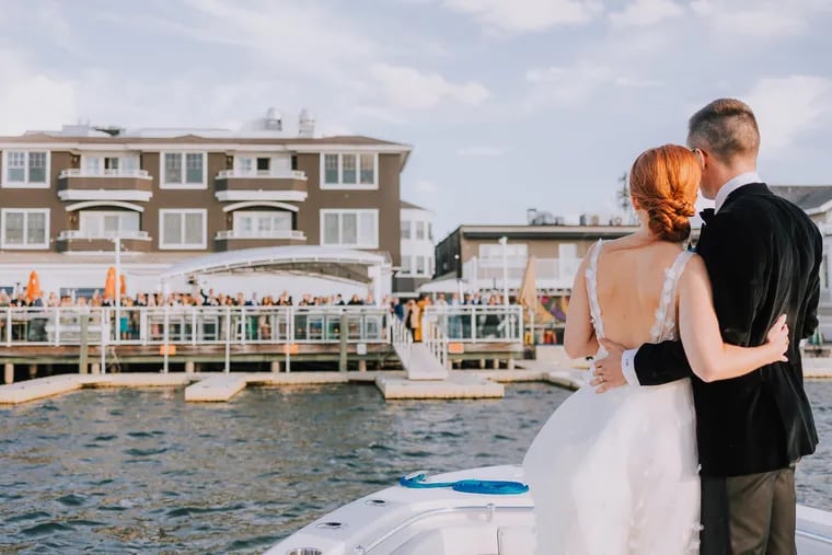 A newly married couple looks out at their wedding guests, who are celebrating on the deck of The Reeds at Shelter Haven in Stone Harbor.