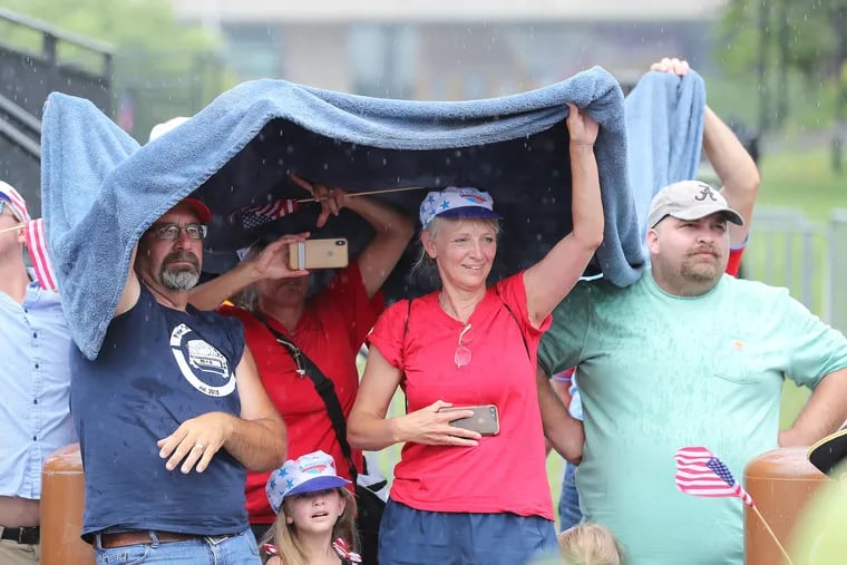 Dan Sachs (left) and his wife, Sharon Sachs (right), take cover as rain falls during the Wawa Welcome America Salute to Independence Day Parade on Tuesday. More showers are due Sunday.