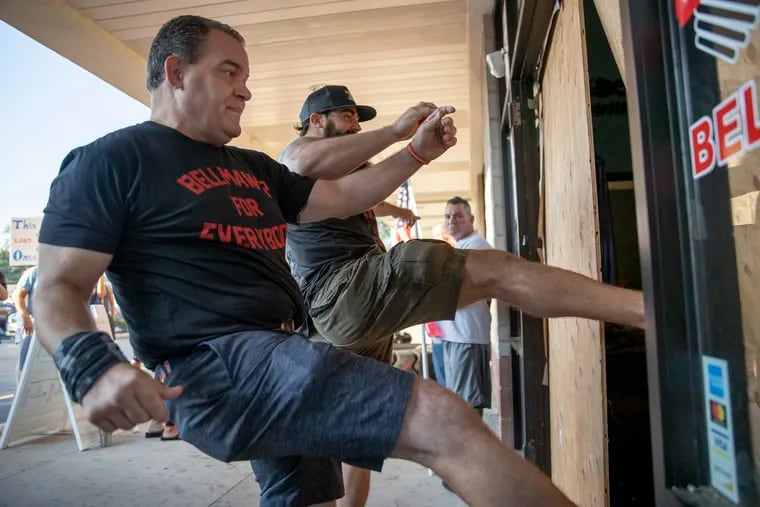 Atilis Gym owners Frank Trumbetti (left) and Ian Smith kick down wooden boards covering the entrance to the facility in Bellmawr on Saturday. Law enforcement officials boarded up the entrance and arrested the owners Monday after they defied a court order to stop operating the gym in violation of state coronavirus restrictions.