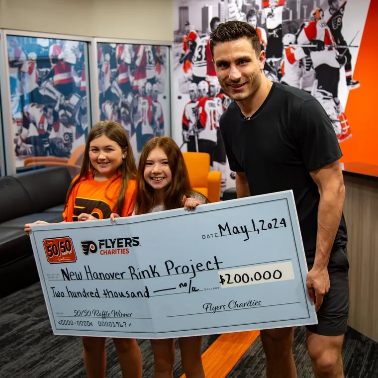 Flyers forward Garnet Hathaway presents Lilly Walter (left) and Natalie Van Druff (middle) with a donation to refurbish their local hockey rink.