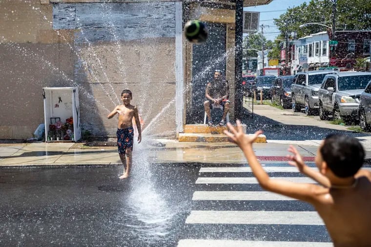 Brothers Xavier, 8, (left) and Julien, 7, (right) with their dad, William McGoldrick, of Huntington Park, as they play football in the street with their neighbor as water sprays out from a fire hydrant on a red-hot Saturday, July 23, 2022.