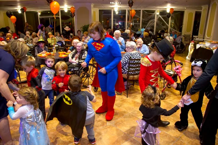 Pat DeHart, dressed as Supergirl, dances with youngsters at Spring Hills Cherry Hill assisted living community as they celebrate Halloween with a family-friendly festival. DeHart, of Cherry Hill, visits her mother, Doris Margo, there twice a week, and for the party Wednesday brought along nine great grandchildren.
