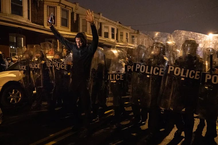 Sharif Proctor, front, raises his hands in the air in front of police as people gather in protest on the 5400 block of Pine Street, in response to the police shooting of Walter Wallace Jr. on Monday., October 26, 2020, in Philadelphia.
