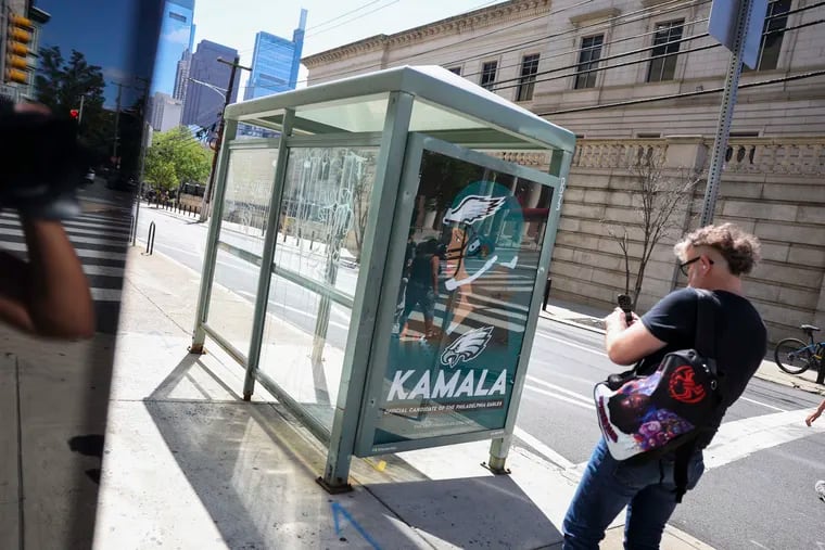 A pedestrian stops at a bus shelter at 16th and Spring Garden Streets on Monday to look at a counterfeit ad claiming Kamala Harris is the official candidate of the Philadelphia Eagles.