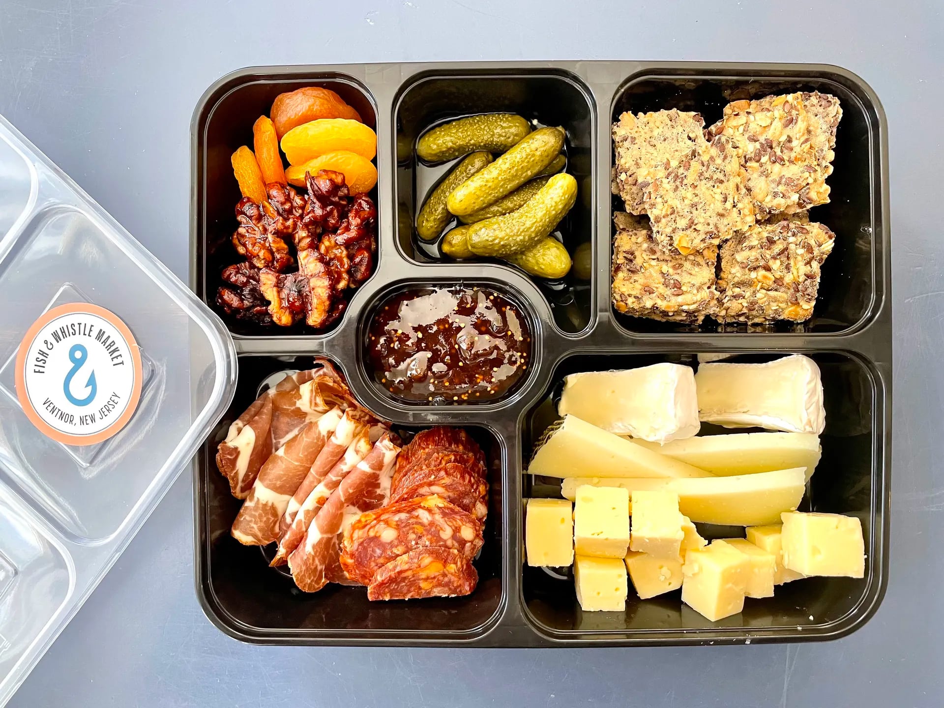 A Snackle Box from Fish & Whistle Market in Ventnor City features cured meats and artisan cheeses with gluten-free crackers, fig jam pickles, and mustard for a charcuterie board to-go.