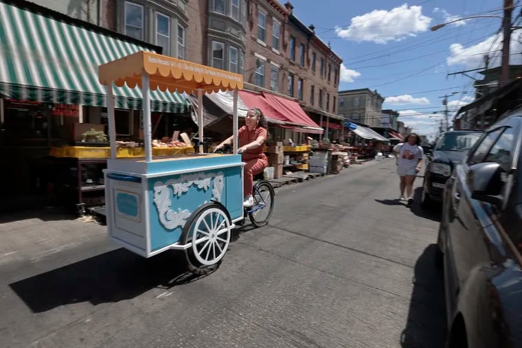 Local artist Michelle Angela Ortiz maneuvers the Our Market cart through the Italian Market in Philadelphia on Saturday, June 15, 2024. Local artist Michelle Angela Ortiz is collecting stories of the immigrant/migrant vendors, business owners, and neighbors who work and reside in the Ninth Street Market for a public art project titled Our Market. The Our Market cart carries all of the tools they need to do interviews and collect information from the public.