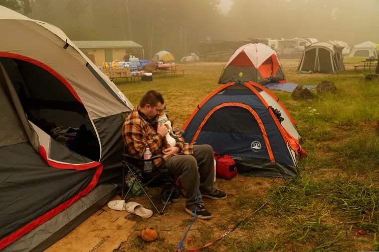 Kristopher Smith holds his dog Tripp outside his tent at an evacuation center at the Milwaukie-Portland Elks Lodge, Sunday, Sept. 13, 2020, in Oak Grove, Ore. Smith evacuated from Molalla, Oregon which was threatened by the Riverside Fire.