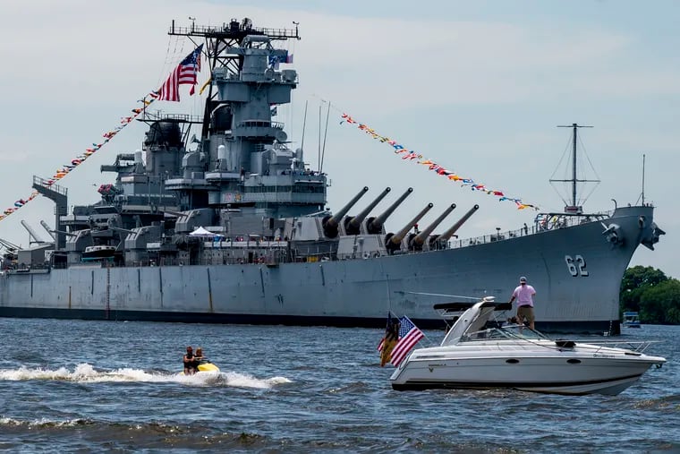 Pleasure watercraft escort the Battleship New Jersey as tugs return it home to the Camden Waterfront Thursday, June 20, 2024, after a restorative hull repainting and other maintenance work in Philadelphia.