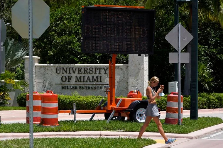In this August 2020 picture, a pedestrian walks past a sign by an entrance to the University of Miami stating that masks, used to prevent the spread of COVID-19, are required to be worn on campus.