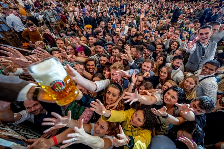 Young people reach out for free beer in one of the beer tents on the opening day of the 187th Oktoberfest beer festival in Munich, Germany, Saturday, Sept. 17, 2022. Not in Munich? Don't worry, Philly has plenty of options too  (AP Photo/Michael Probst)