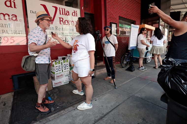 Stuart Rome of Philadelphia (left) is filmed while being interviewed by Our Market project manager Sophia Terry in the Italian Market in Philadelphia on Saturday, June 15, 2024. Local artist Michelle Angela Ortiz is collecting stories of the immigrant/migrant vendors, business owners, and neighbors who work and reside in the Ninth Street Market for a public art project titled Our Market.