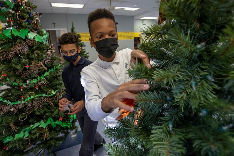 Joshua Harrington, 13, and classmate Dalanie Franklin, 13, (background) work together to decorate a Christmas tree. Norwood Mansion, Norwood-Fonbonne Academy, the Norwood Mansion is the centerpiece of the Chestnut Hill tour this year, 2021. Photograph taken during decoration of Christmas trees on display inside the mansion, Tuesday, November 23, 2021.