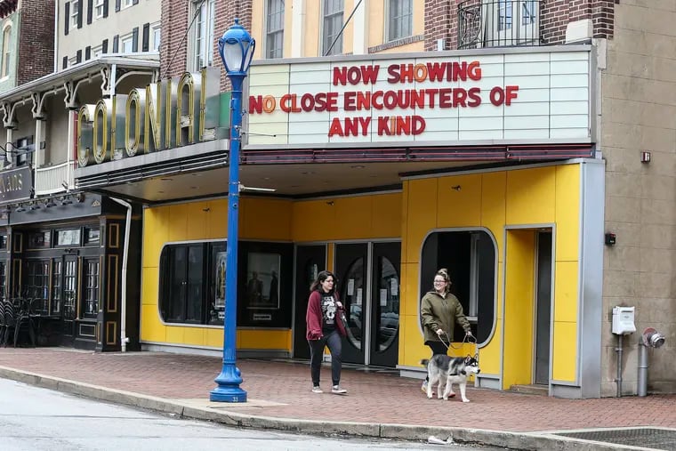 Sydney Kook, walking "Hutch," and Niciole Troia walk under a sign of the times at The Colonial Theatre in Phoenixville on Thursday.