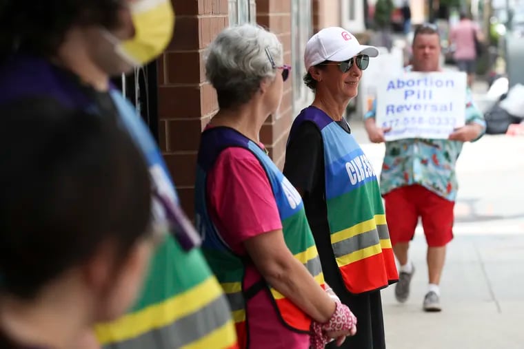 Patient escorts wait outside of the Planned Parenthood Elizabeth Blackwell Health Center in Center City Philadelphia in July 2022 as an anti-abortion protester stands down the street.