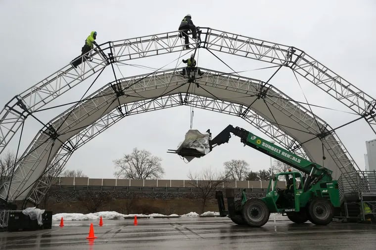 Employees of Mountain Productions construct covered arches to be used as drive-throughs for a COVID-19 vaccination site run by 15toKnow in the parking lot of the former Babies R Us in King of Prussia on Sunday. But it has yet to get state authorization.
