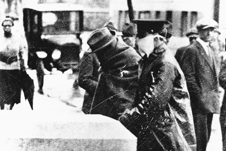 An influenza victim, wrapped in a blanket, being escorted by a policeman, who wears a protective facemask of some sort, during the influenza epidemic in 1918.